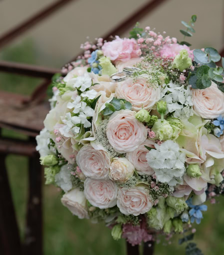 Ein Blumenstrauß mit rosa und weißen Rosen, blauen und grünen Akzenten, liegt auf einem Metallgeländer.